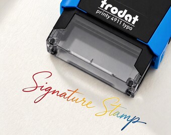 May include: A blue and black Trodat Printy 4911 typo self-inking stamp positioned above the text Signature Stamp, which is printed in a gradient script font transitioning from red to orange, yellow, and blue on a textured white surface.