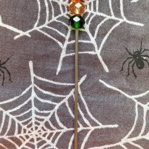 Op de afbeelding: Een zilveren metalen stok met drie glazen kralen. De kralen zijn rood, oranje en groen.