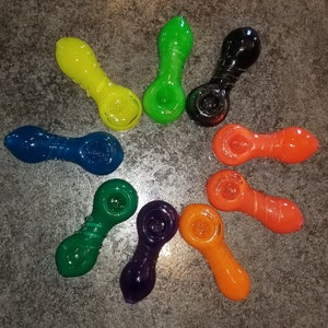 May include: A set of nine colorful glass pipes in various colors, including green, blue, yellow, orange, red, and black. The pipes are arranged in a circle on a gray surface.