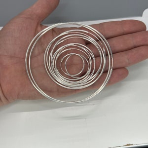 May include: A set of silver hoop earrings of varying sizes, arranged in a circular pattern.