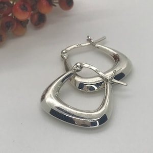 May include: A pair of silver hoop earrings with a unique, slightly curved, triangular shape. The earrings are marked with "925" indicating they are made of sterling silver.