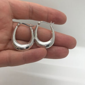 May include: A pair of silver oval hoop earrings. The earrings are smooth and have a polished finish.