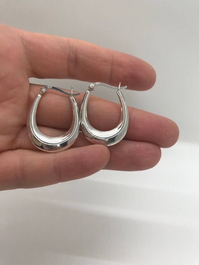 May include: A pair of silver oval hoop earrings. The earrings are smooth and have a polished finish.