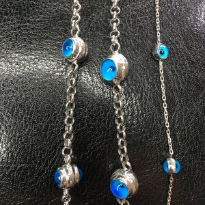May include: Three silver chains with blue evil eye charms. The chains are of varying lengths and the charms are different sizes.