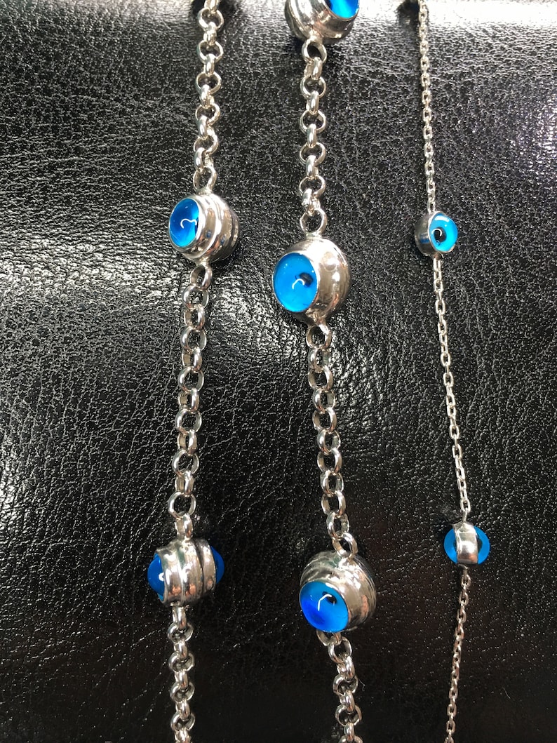 May include: Three silver chains with blue evil eye charms. The chains are of varying lengths and the charms are different sizes.