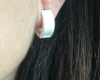 May include: Silver hoop earrings with a brushed finish. The earrings are shown in a person's ear.