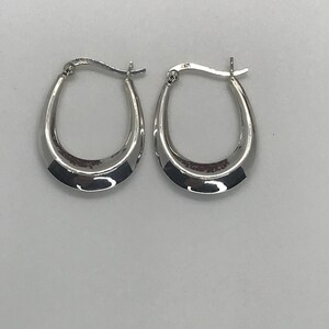 May include: A pair of silver hoop earrings with a slightly curved shape.