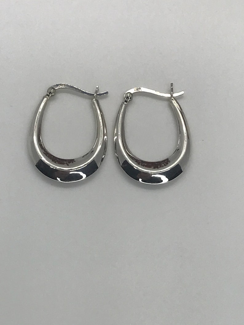 May include: A pair of silver hoop earrings with a slightly curved shape.