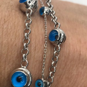 May include: A silver chain bracelet with multiple blue evil eye charms. The charms are round and have a silver setting.