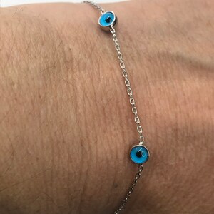 May include: A silver chain bracelet with three blue evil eye charms.
