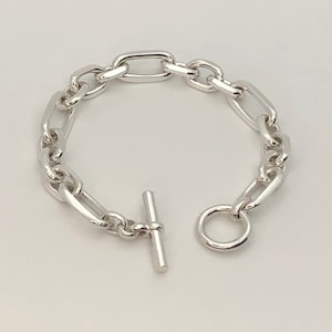 Könnte beinhalten: Ein silbernes Kettenarmband mit einem Toggle-Verschluss. Die Kette besteht aus großen, ovalen Gliedern.