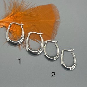 May include: Three pairs of silver hoop earrings of different sizes. The earrings are arranged in order of size, with the largest pair on the left and the smallest pair on the right. The earrings are all oval shaped and have a smooth, polished finish.