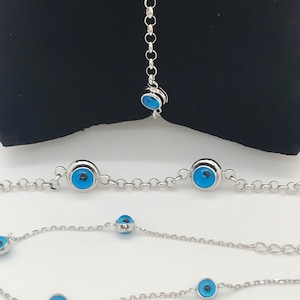 May include: Three silver chain bracelets with blue evil eye charms. The bracelets are of different lengths.