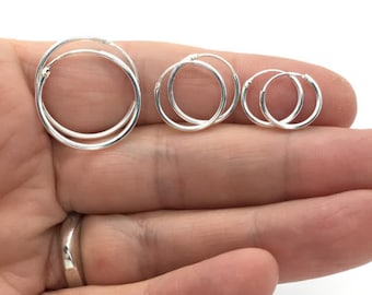 May include: Three silver hoop earrings of different sizes. The earrings are shown on a hand.