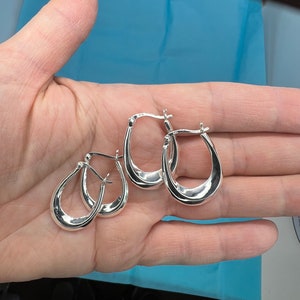 May include: Three silver hoop earrings with a slightly curved shape. The earrings are all the same size and style.