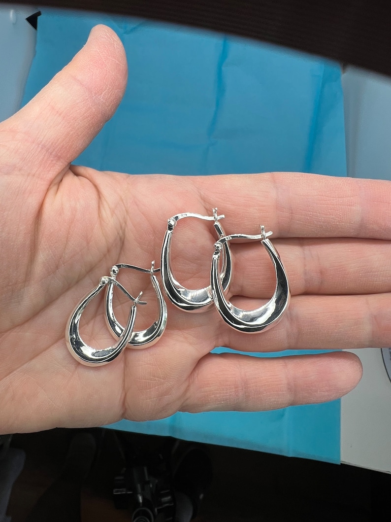 May include: Three silver hoop earrings with a slightly curved shape. The earrings are all the same size and style.