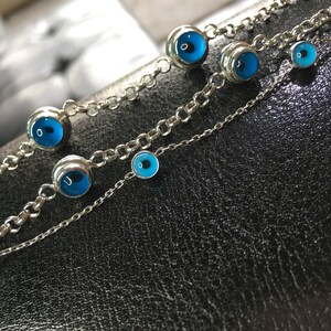 May include: Three silver chain bracelets with blue evil eye charms. The charms are different sizes and are set in silver.
