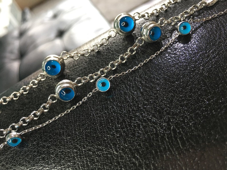 May include: Three silver chain bracelets with blue evil eye charms. The charms are different sizes and are set in silver.