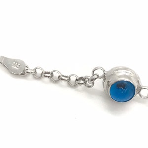 May include: A silver chain bracelet with a blue gemstone pendant. The pendant is round and has a silver setting. The chain is made of small, linked circles.