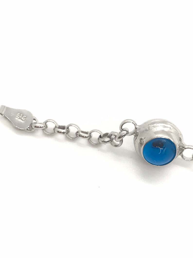 May include: A silver chain bracelet with a blue gemstone pendant. The pendant is round and has a silver setting. The chain is made of small, linked circles.