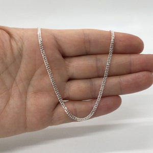 Può includere: Una collana a catena curb in argento. La catena è lunga circa 45 cm e ha un design delicato e piatto.
