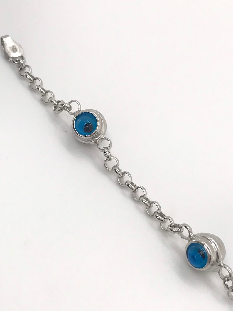 May include: A silver chain bracelet with three blue evil eye charms. The bracelet is made of a delicate chain and the charms are round with a blue glass center.