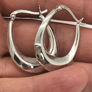 May include: A pair of silver oval hoop earrings. The earrings are smooth and have a slightly curved shape.