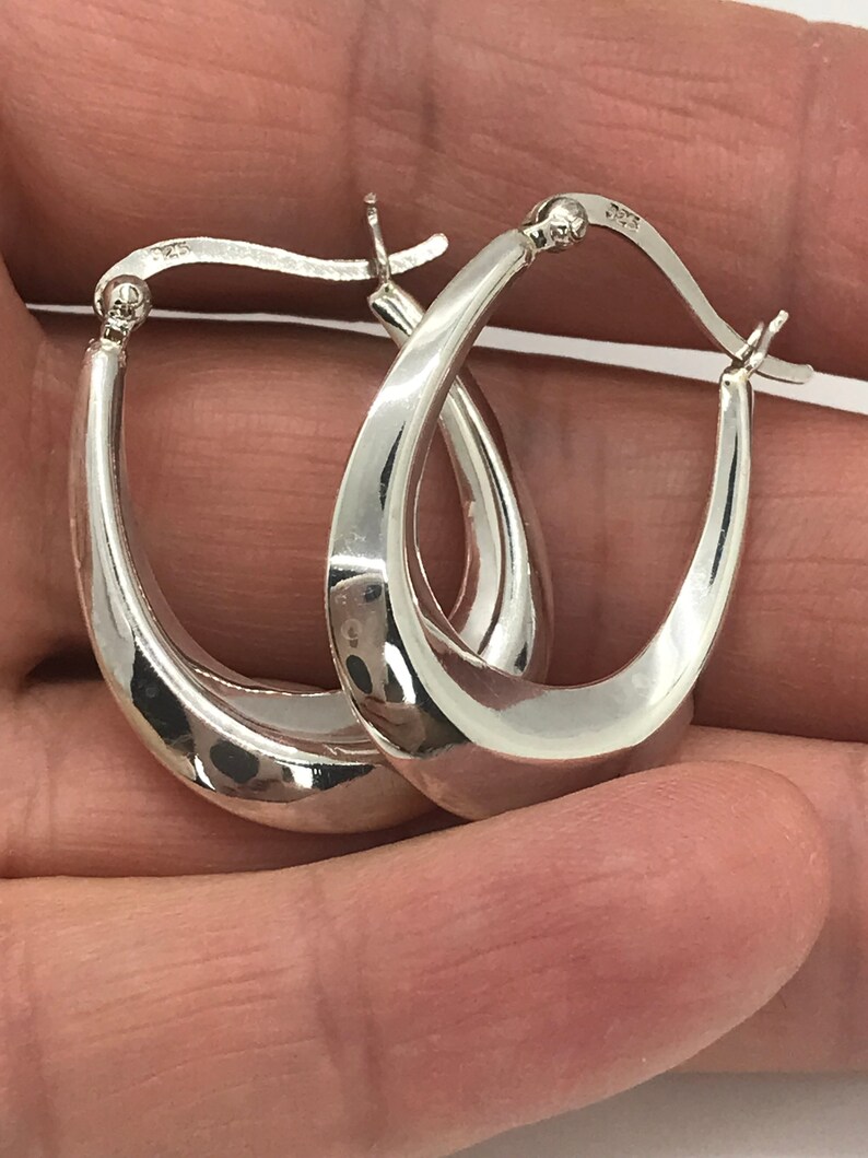 May include: A pair of silver oval hoop earrings. The earrings are smooth and have a slightly curved shape.