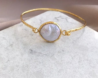 Puede incluir: Un brazalete de oro con una perla grande, blanca e irregular engastada en un engaste de oro.