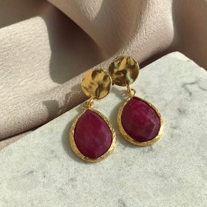 Può includere: Un paio di orecchini dorati con accenti di pietre preziose rosse a forma di goccia.