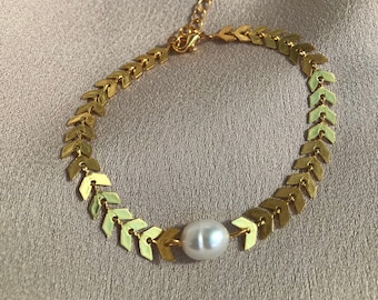 May include: A gold chain bracelet with a single white pearl accent. The chain is made of small arrow-shaped links.