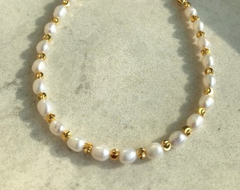 May include: A delicate gold chain bracelet with small white pearls and gold beads. The bracelet has an adjustable sliding clasp.