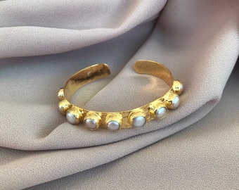 Puede incluir: Un brazalete de oro con acabado martillado y detalles de perlas blancas.