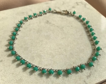 May include: A silver chain bracelet with small, dangling turquoise blue beads.