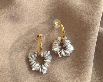 May include: A pair of gold hoop earrings with a heart-shaped design made of small, white pearl-like beads.