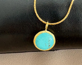 Peut inclure: Un collier en chaîne dorée avec un pendentif en pierre turquoise. Le pendentif est rond et a une bordure dorée.