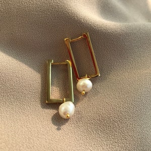 May include: A pair of gold hoop earrings with a small white pearl dangling from each hoop.