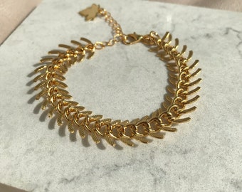 Könnte beinhalten: Ein goldenes Kettenarmband mit einem einzigartigen, spitzen, blattartigen Design. Das Armband hat einen Karabinerverschluss und einen kleinen Schmetterlingsanhänger.