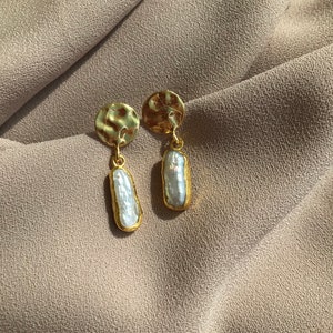 Peut inclure: Une paire de boucles d'oreilles en or avec un disque rond texturé et une perle baroque blanche pendante.