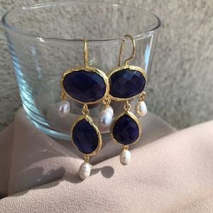 Puede incluir: Pendientes de oro con una piedra preciosa azul oscuro y detalles de perlas blancas.