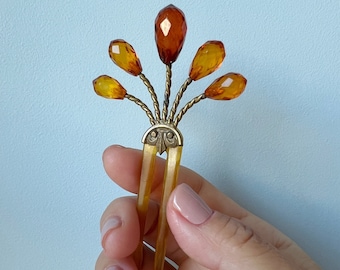 May include: A gold and amber hair comb with a decorative design and five amber glass beads.