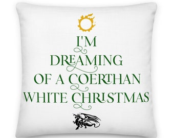 Könnte beinhalten: Weißes quadratisches Kissen mit dem Text "I'M DREAMING OF A COERTHAN WHITE CHRISTMAS" in Grün, mit einem goldenen Sonnensymbol und einer schwarzen Drachenillustration. Ein dekorativer Artikel für das Zuhause.