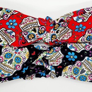 May include: Two fabric headbands with a sugar skull pattern. One headband is red with white and blue skulls, the other is black with white and blue skulls.