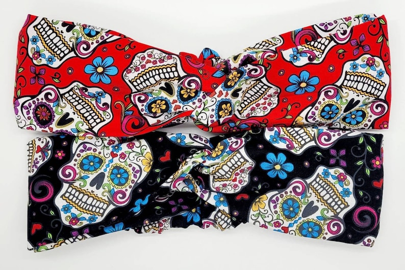May include: Two fabric headbands with a sugar skull pattern. One headband is red with white and blue skulls, the other is black with white and blue skulls.
