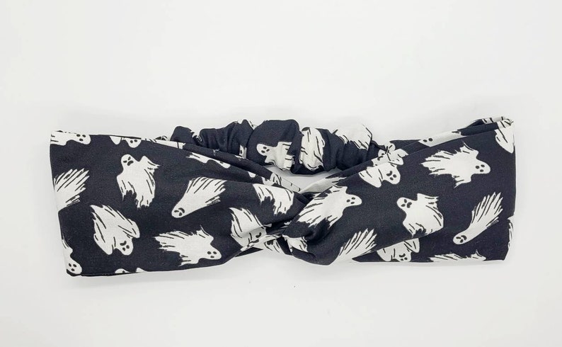 May include: Black headband with a white ghost pattern. The headband is twisted and has a gathered elastic section in the back.