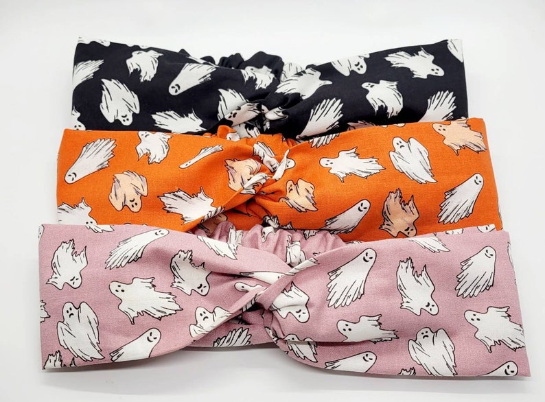 May include: Three fabric headbands with a ghost pattern. The headbands are black, orange, and pink. Each headband has a knotted design.