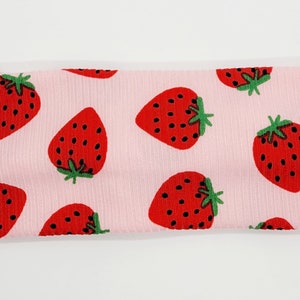 May include: Pink headband with a repeating pattern of red strawberries on a pink background.