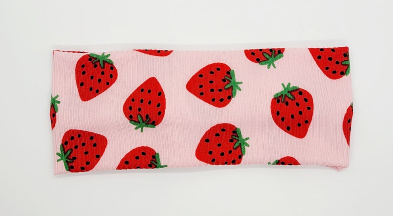 May include: Pink headband with a repeating pattern of red strawberries on a pink background.