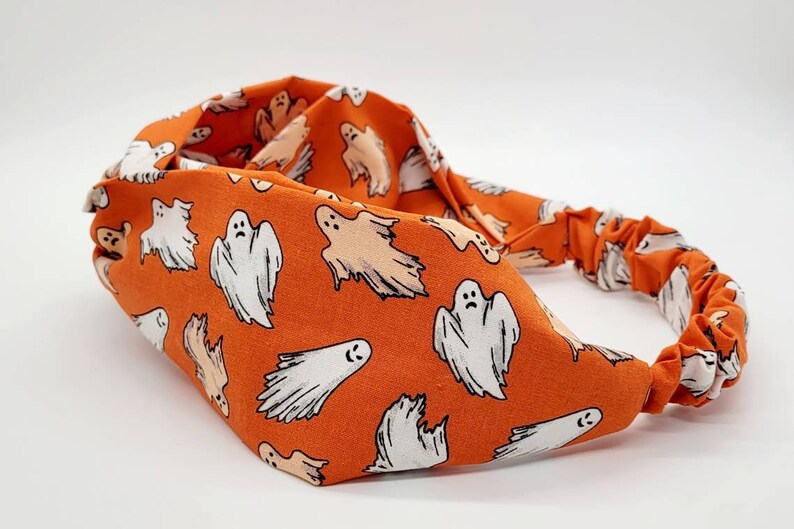 May include: Orange headband with a white ghost pattern. The headband is made of a soft, stretchy fabric and is perfect for adding a touch of spooky fun to any outfit.