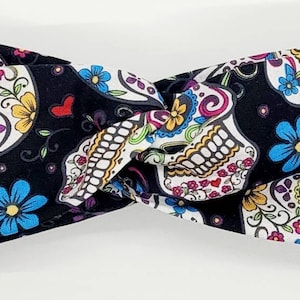 May include: A black headband with a white and colorful sugar skull pattern. The headband is twisted and has a knot in the center.